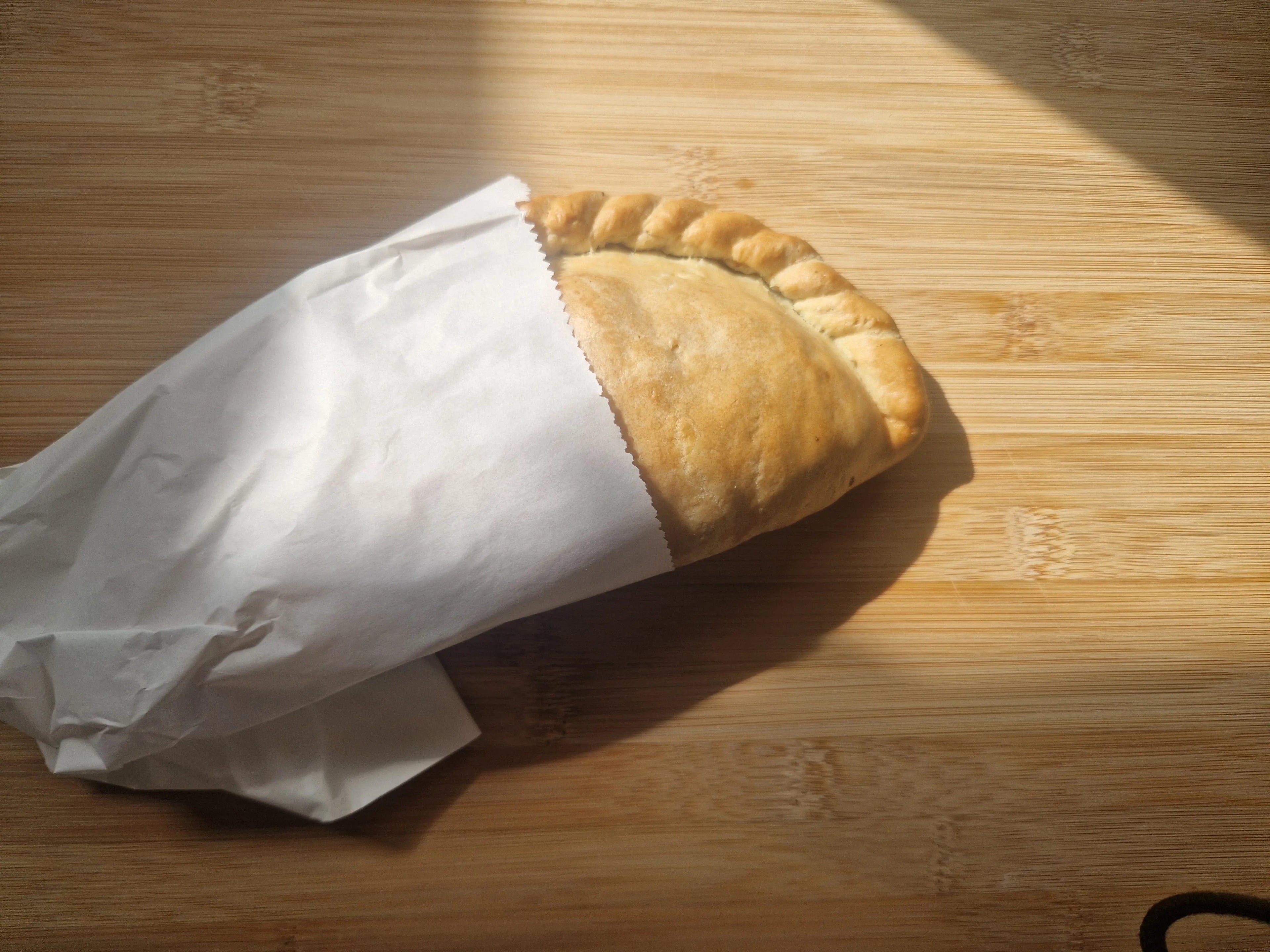 Baked soya mince vegan pasty wrapped in white paper on a wooden surface