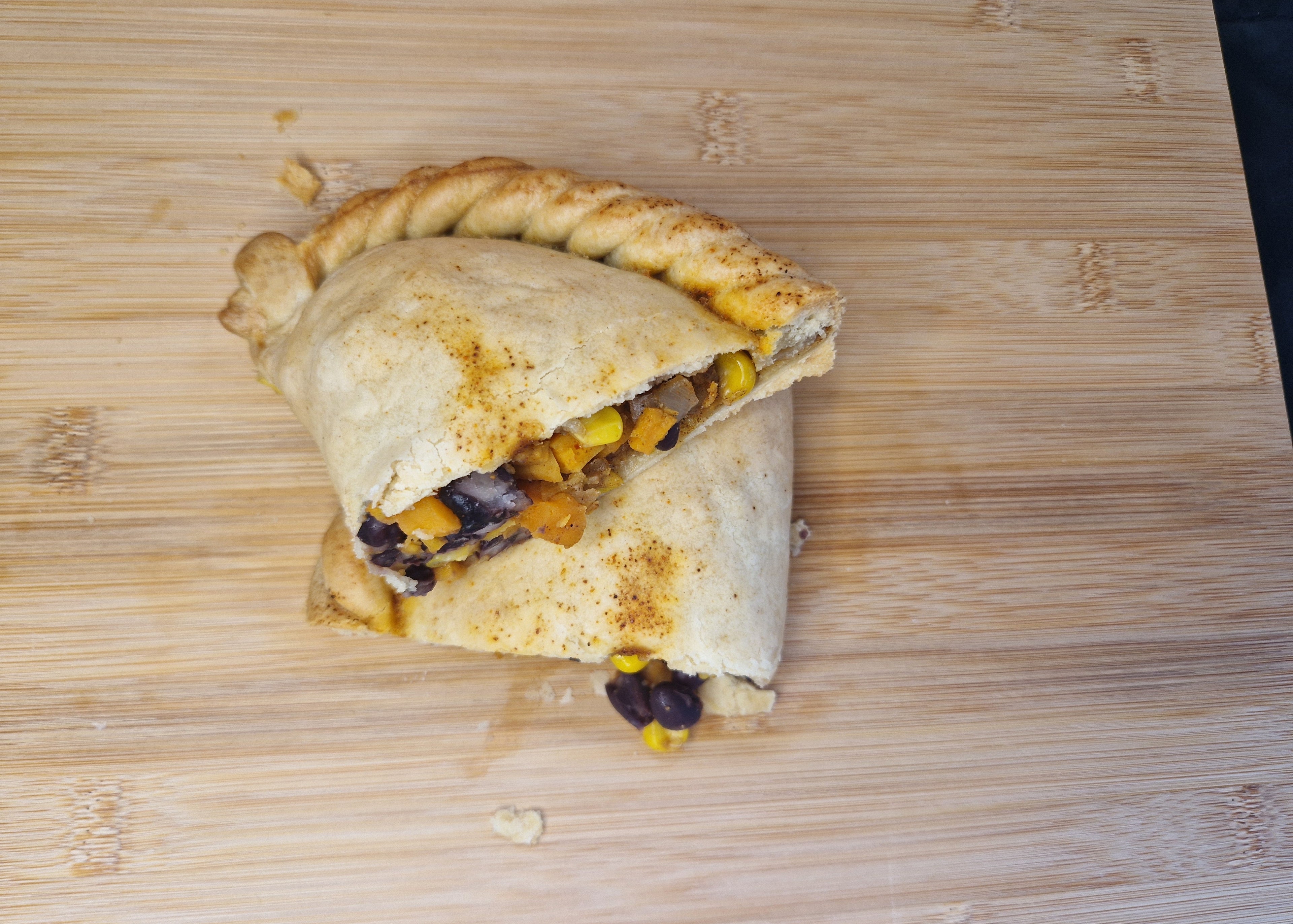 Sweet potato pasty cut in half on a wooden cutting board