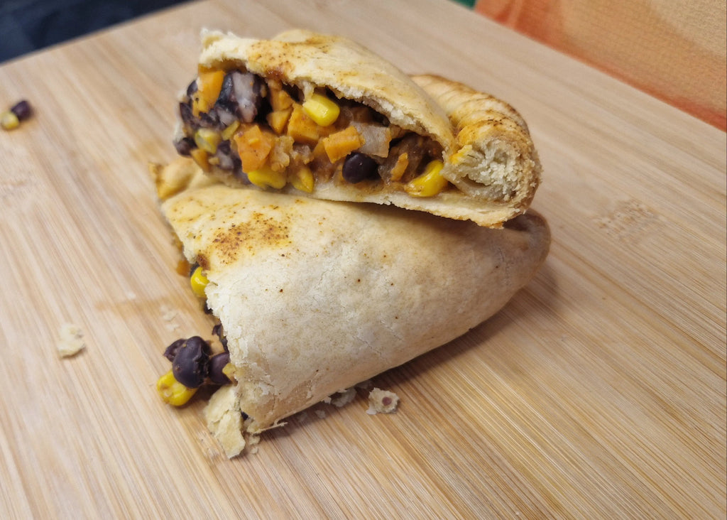 vegan pasty cut in half showing sweet potato, black bean, and sweetcorn filling on a wooden cutting board
